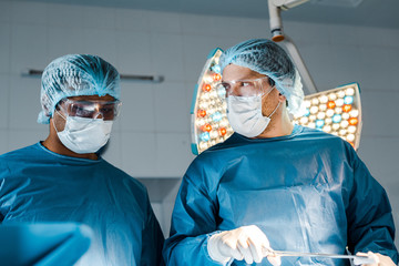 nurse and surgeon in uniforms and medical masks doing operation