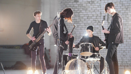 A young rock group having a repetition in a hangar. Members of a group wearing black clothes. Bright lighting