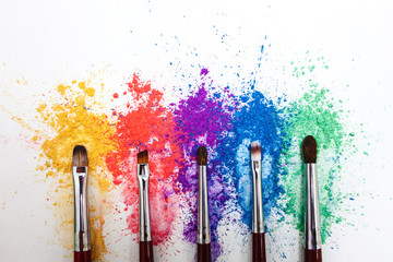 Bright eye shadows in different colors of the rainbow and brushes for cosmetics on a white background.