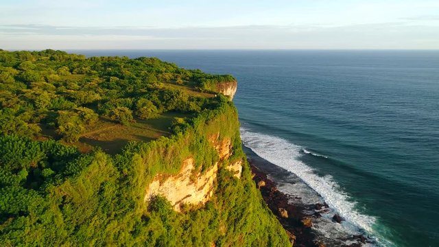 Aerial, drone shot flying parallel to the Karang boma cliff with incredible ocean view, towards people on the ledge, on a sunny evening, in Uluwatu, in Bali, Indonesia - 4k Footage