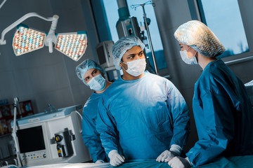 doctors and nurse in uniforms and medical masks talking in operating room