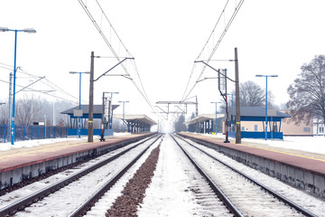 Empty train station in the middle of a winter, train tracks covered by snow. 