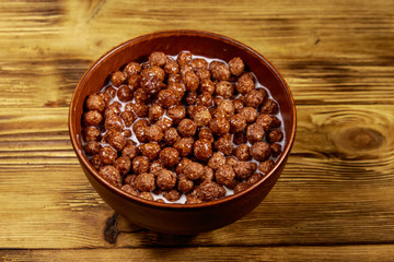 Cereal chocolate balls with milk in a bowl on wooden table