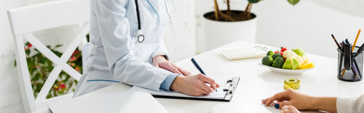 panoramic shot of nutritionist writing diagnosis near patient