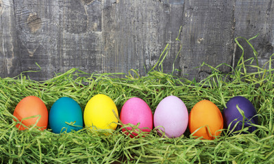 Colorful Easter eggs on green grass on wooden background. Easter or egg hunt concept