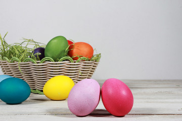 Colorful eggs in basket on white wooden table. Easter concept. Colored eggs, isolated on white