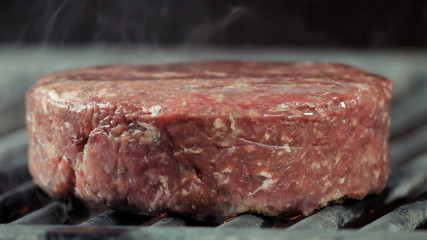The beginning of cooking cutlets, close-ups on the side of a large grilling cutlet on the grill a little smoked, beef or calf meat formed in a cutlet