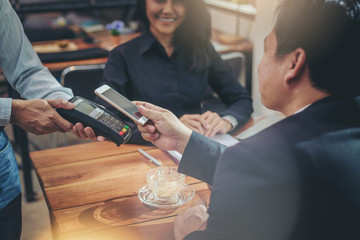 Businessman paying with NFC technology by smartphone in coffee shop. mobile QR code payment concept