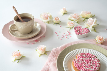 rusk with pink and white aniseed, Dutch Muisjes. Traditional treat when a baby girl is born in The Netherlands. Cup of tea and roses on white table.