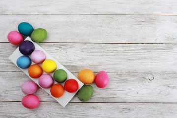 Obraz premium Easter concept. Egg rack with and scattered colorful eggs on white wooden table. Pink, yellow, green, orange, blue, violet