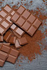 Dark or milk organic chocolate pieces and cocoa powder on dark concrete backgound