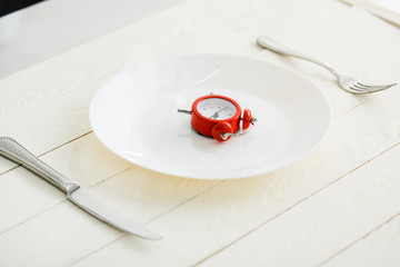 white plate with cutlery near red alarm clock on wooden surface