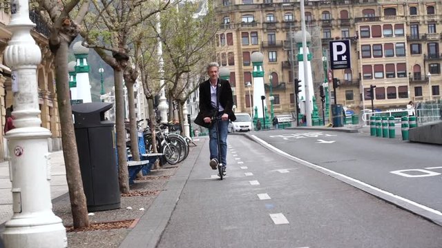 Slow motion of businessman commuting to work on micro scooter