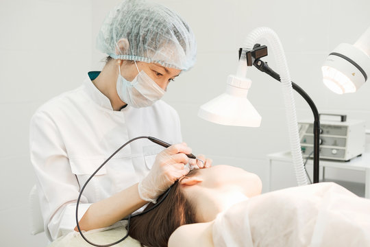 Medical treatment removal of birthmark from female patient's face. Female dermatologist surgeon using a professional electrocautery for removing mole. Radio wave electrocoagulation remove method