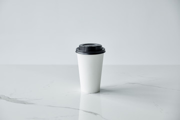 white paper cup with black cap on white marble surface isolated on grey