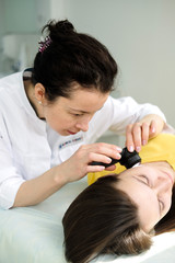 Female dermatologist using a professional dermatoscope while doing skin examination, Checking...