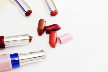 pieces of broken lipstick and open cases lie side by side on a white background