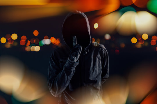 Hooded maniac with finger on lips gesturing shh sign