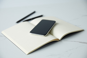 selective focus of smartphone with blank screen on notebook, pen and pencil on white surface