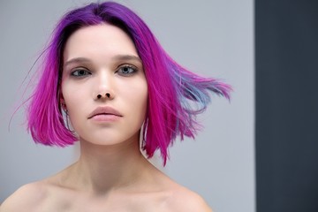 Naklejka premium Concept Portrait of a punk girl, young woman with chic purple hair color in studio close up on a colorful background with fluttering hair.