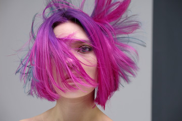 Concept Portrait of a punk girl, young woman with chic purple hair color in studio close up on a colorful background with fluttering hair.
