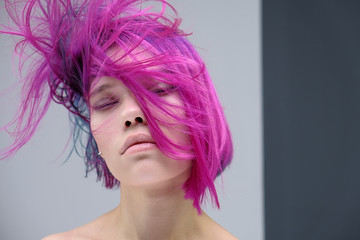 Concept Portrait of a punk girl, young woman with chic purple hair color in studio close up on a colorful background with fluttering hair.