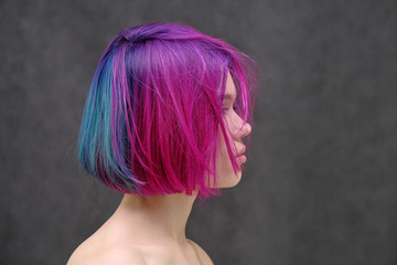 Concept Portrait of a punk girl, young woman with chic purple hair color in studio close up on a colorful background with fluttering hair.