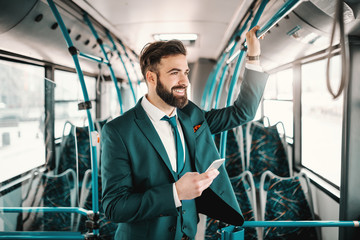 Smiling Caucasian businessman in suit driving in public bus and using smart phone. You only fail...