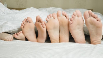 Family feet in bed under white blanket - Powered by Adobe