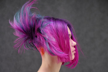Concept Portrait of a punk girl, young woman with chic purple hair color in studio close up on a colorful background with fluttering hair.