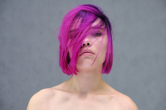 Concept Portrait of a punk girl, young woman with chic purple hair color in studio close up on a colorful background with fluttering hair.