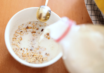 Close up of pregnant woman in apron pouring milk in bowl with oats.