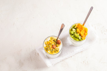 Two glasses with yogurt and fruit puree and with metallic spoons are standing diagonally on white background.