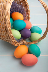 Fototapeta na wymiar Mix of dyed bright Easter eggs in a withe basket with colorful blue sisal on a wooden blue surface., selective focus..