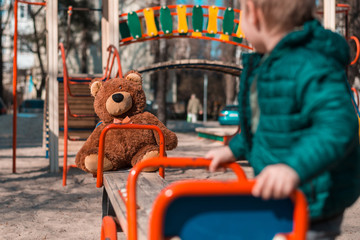 A little boy is playing on a playground with a teddy bear.