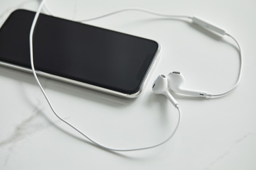 smartphone with blank screen and wired earphones on white marble surface