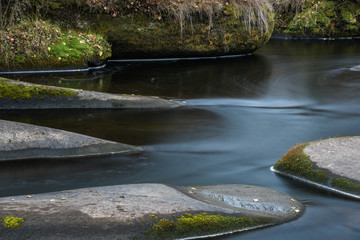 Long exposure shot of the dark flowing river among the stones with green moss