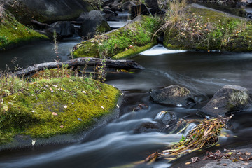 Long exposure shot of the dark flowing river among the stones with green moss