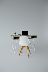 white chair, table with laptop, books and flowerpot on grey background