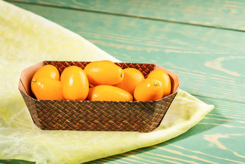 Cardboard box with  kumquats on yellow fabric on diagonal green wooden background.
