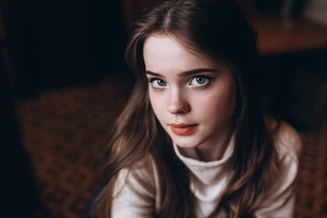 Fototapeta premium Cheerful young girl's portrait having breakfast at cozy home with big cup of coffee or tea holding in hands sitting near window and dreaming. Lifestyle, relaxation, natural beauty, teenage age concept