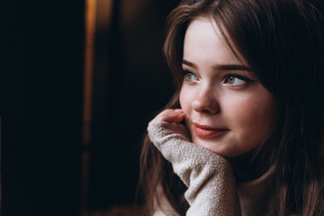 Cheerful young girl's portrait having breakfast at cozy home with big cup of coffee or tea holding in hands sitting near window and dreaming. Lifestyle, relaxation, natural beauty, teenage age concept