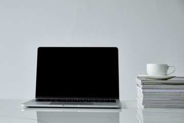 laptop with blank screen and coffee cup on stacked journals isolated on grey