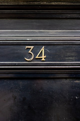 Obraz premium House number 34 with the thirty-four in bronze numbers on a black wooden door with parallel lines