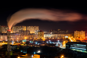 Telephoto lens long exposure shot of night cityscape with pipe and chimney emitting steam or smoke