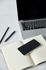 selective focus of smartphone with blank screen, notebook and laptop on white surface