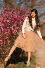 Young beautiful teen girl with perfect skin is wearing romantic clothes posing near blossom tree in cherry garden