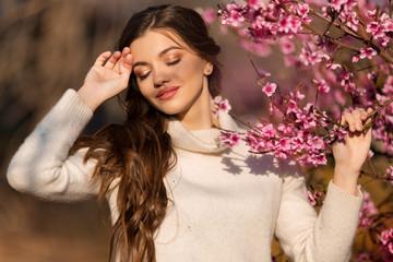 Obraz na płótnie Canvas Young beautiful teen girl with perfect skin and makeup is wearing romantic clothes posing near blossom tree in cherry garden