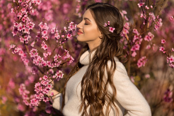 Naklejka premium Young beautiful teen girl with perfect skin and makeup is wearing romantic clothes posing near blossom tree in cherry garden
