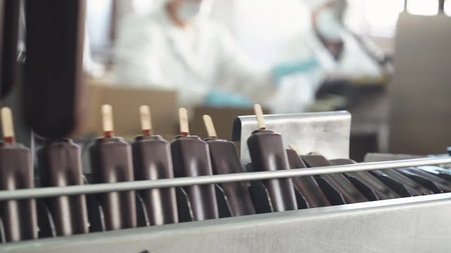 ice cream production, chocolate ice cream is transported on a conveyor, dairy products, workers on blurred background.